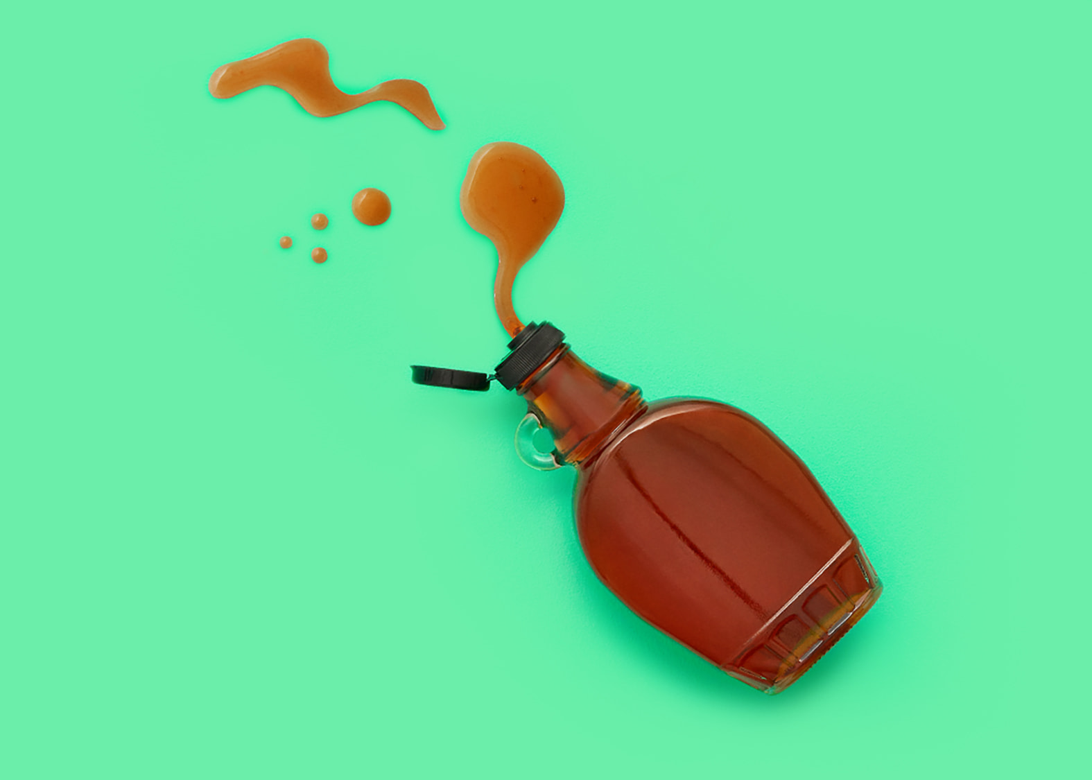 Green background with spilled maple syrup coming out of a glass bottle.