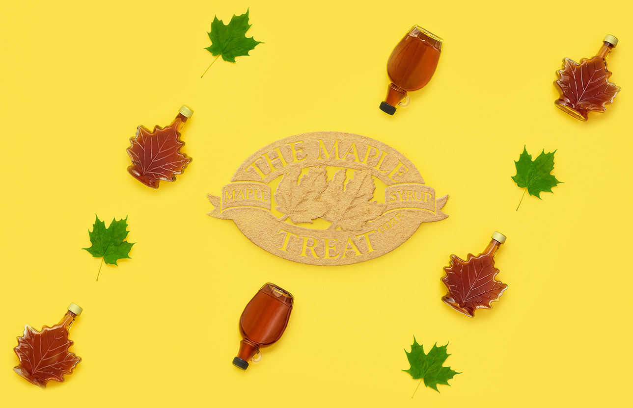 Logo pochoir fait de sucre d’érable The Maple Treat Corp. avec des bouteilles de sirop d’érable et des feuilles d’érable qui l’entourent.