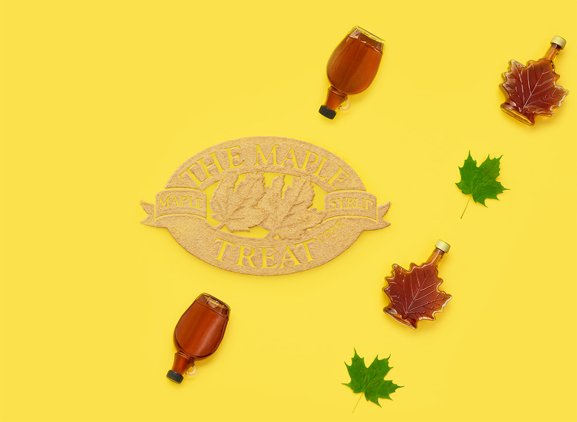 Logo The Maple Treat Corp. en pochoir fait avec du sucre d’érable, avec des bouteilles de sirop d’érable et des feuilles d’érable qui l’entourent.