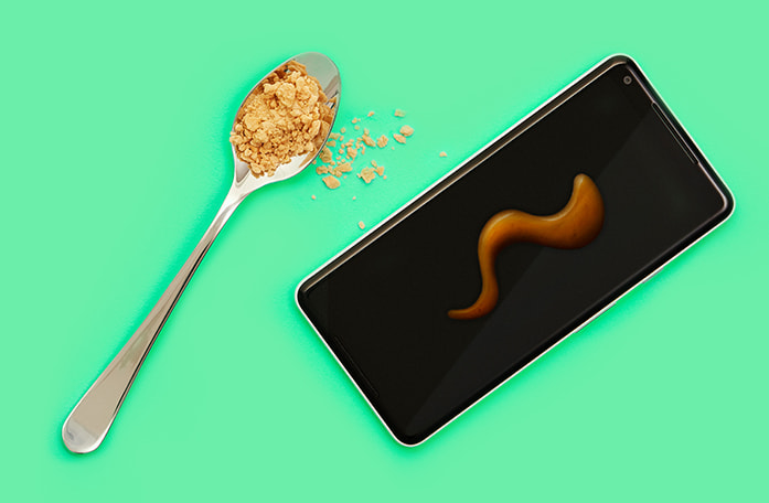Spoon filled with maple flakes beside a cell phone with maple syrup swirled on top.
